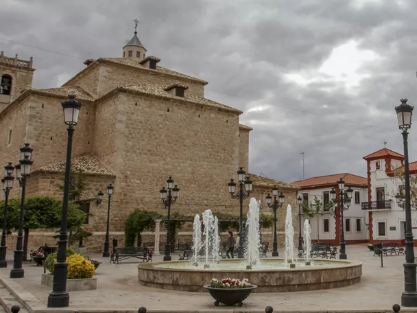 Plaza histórica manchega con iglesia de piedra y ayuntamiento.