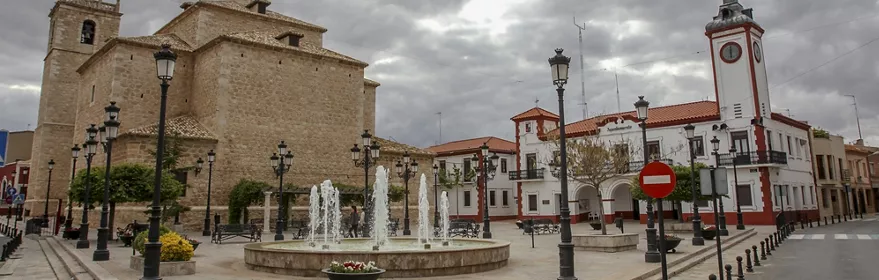 Plaza histórica manchega con iglesia de piedra y ayuntamiento.
