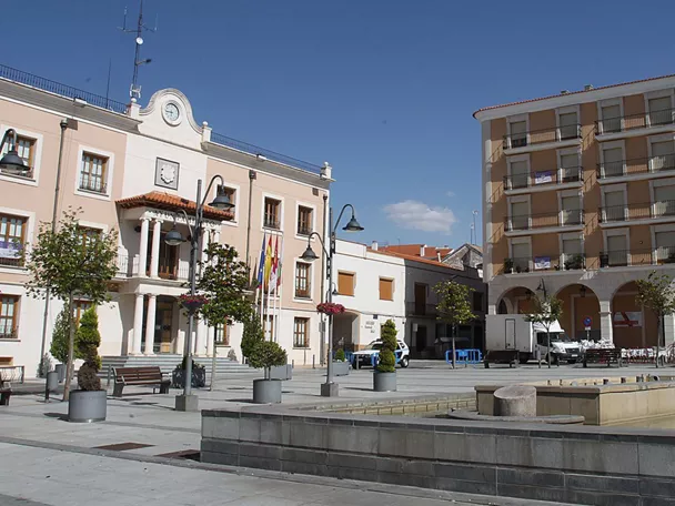 Plaza principal con ayuntamiento y fuente en un día soleado.