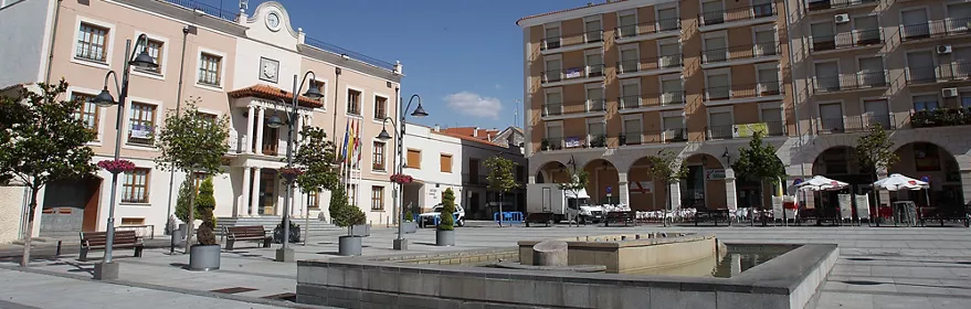 Plaza principal con ayuntamiento y fuente en un día soleado.