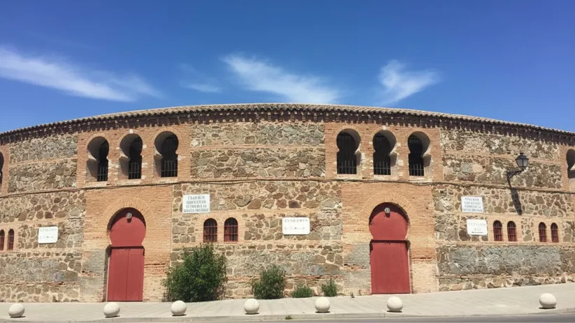 Plaza de toros de piedra con arcos y puertas rojas