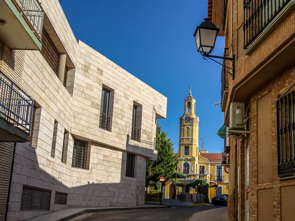 Calle urbana con edificios y torre amarilla con reloj al fondo