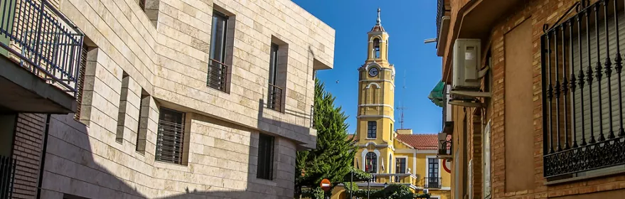 Calle urbana con edificios y torre amarilla con reloj al fondo