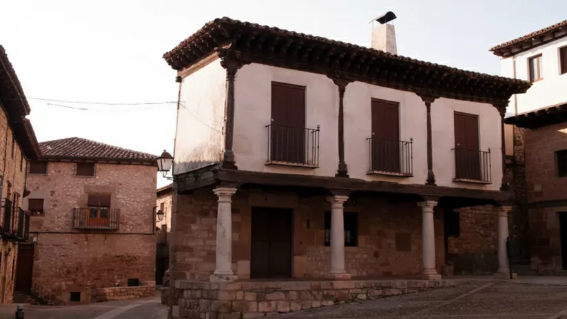 Vivienda tradicional con columnas de piedra y balcones en esquina de plaza.