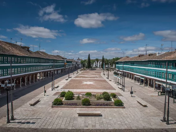 Plaza porticada con balcones verdes y espacio central empedrado