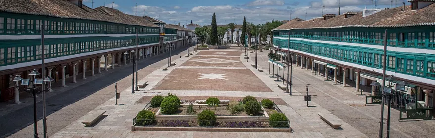 Plaza porticada con balcones verdes y espacio central empedrado