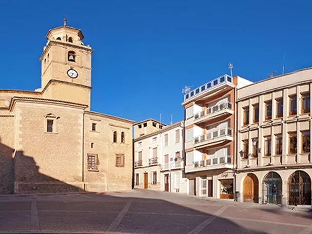 Vista panorámica de una plaza amplia con edificio institucional de cúpula azul y torre de piedra a un lado.