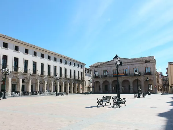  Plaza porticada con bancos y farolas bajo cielo despejado                   