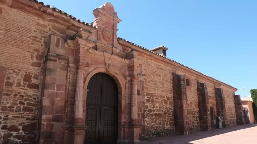 Fachada de piedra con portada barroca y puerta de madera.