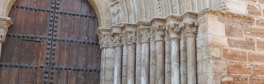 Detalle de portada románica con columnas y puerta de madera.