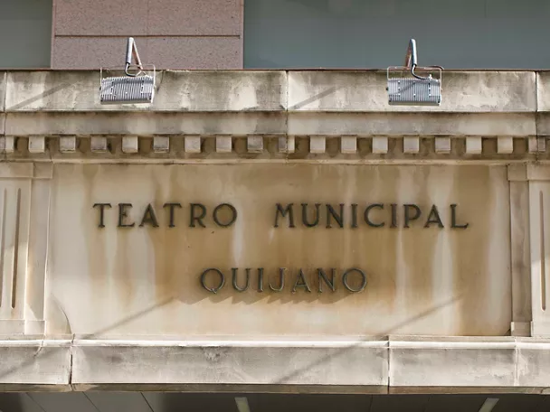 Fachada de teatro con inscripción en piedra y luminarias superiores.