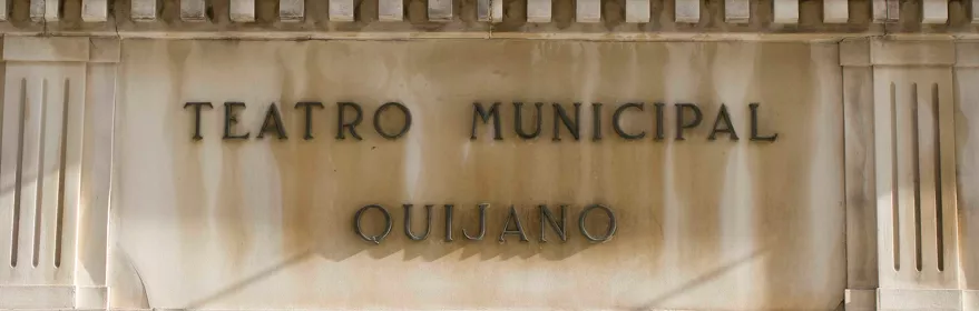 Fachada de teatro con inscripción en piedra y luminarias superiores.