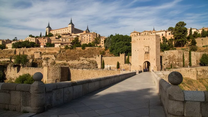 Puente de piedra hacia puerta fortificada y ciudad en la colina