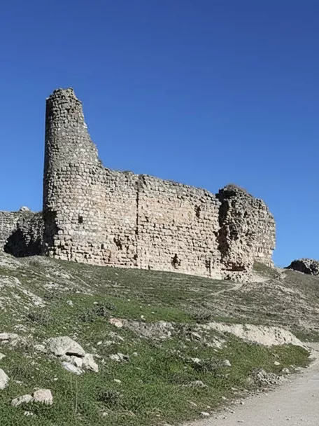 Ruinas de fortaleza sobre colina junto a camino.
