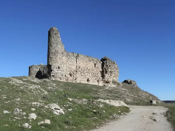 Ruinas de fortaleza sobre colina junto a camino.