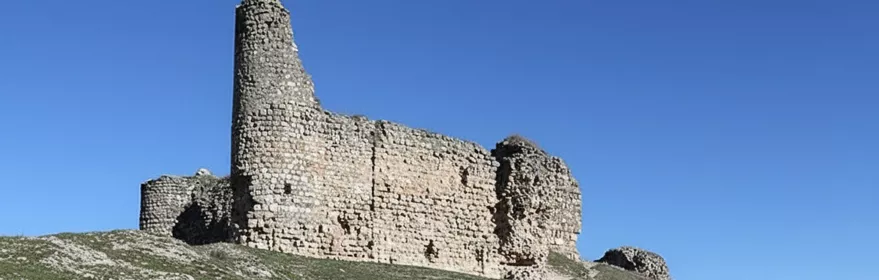 Ruinas de fortaleza sobre colina junto a camino.
