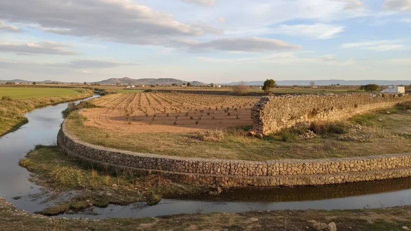Campos de cultivo junto a un canal de piedra con montañas al fondo.