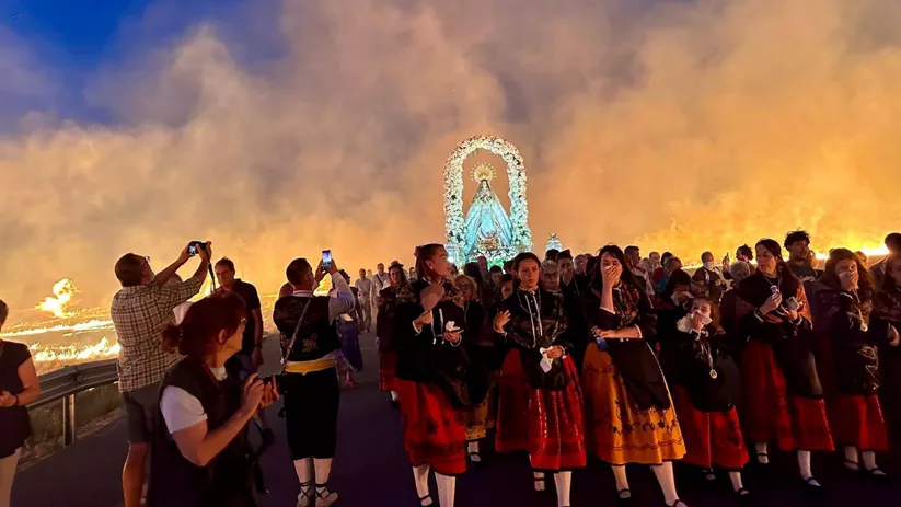 Procesión con imagen religiosa entre llamas y humo.