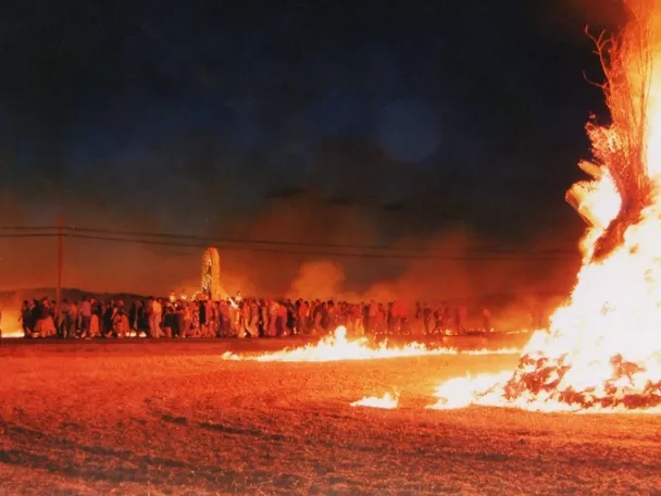 Hoguera nocturna con multitud reunida en el campo.