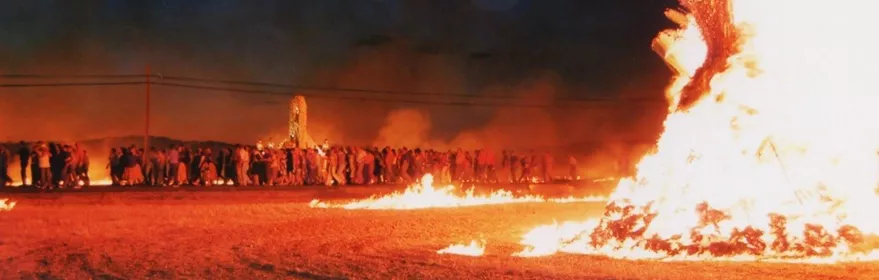 Hoguera nocturna con multitud reunida en el campo.