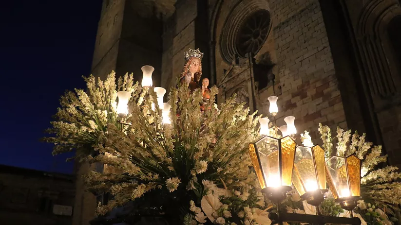 Imagen religiosa iluminada con flores ante fachada nocturna.