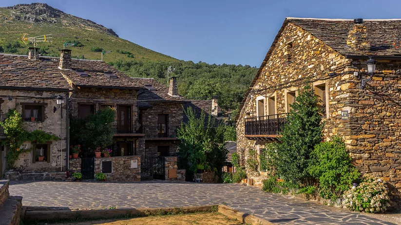 Plaza empedrada rodeada de casas de piedra con montaña al fondo.
