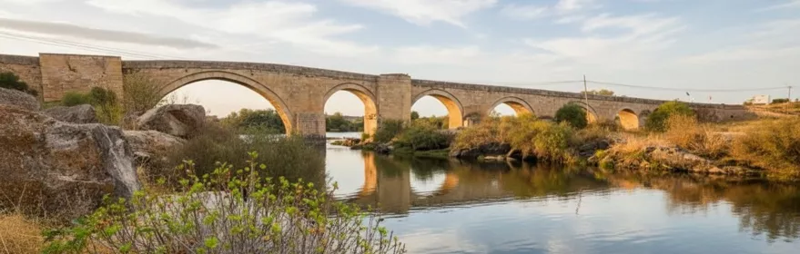 Puente de piedra sobre río con arcos y reflejos