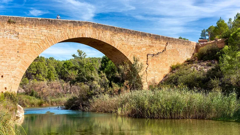 Puente de piedra de un solo arco sobre un río.