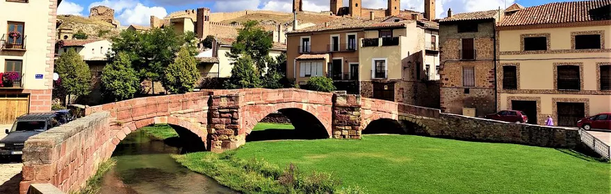 Puente de piedra sobre río con murallas al fondo.