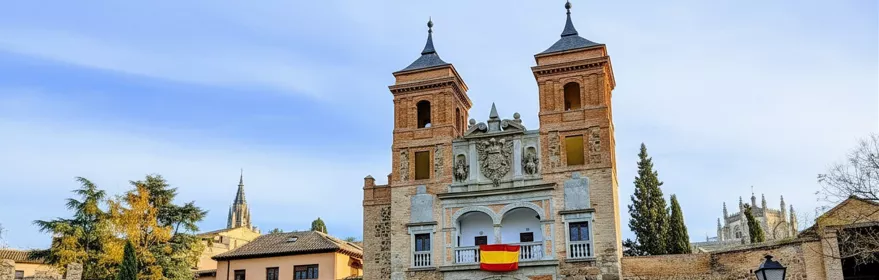 Puerta amurallada con bandera en el balcón y calle empedrada al fondo.