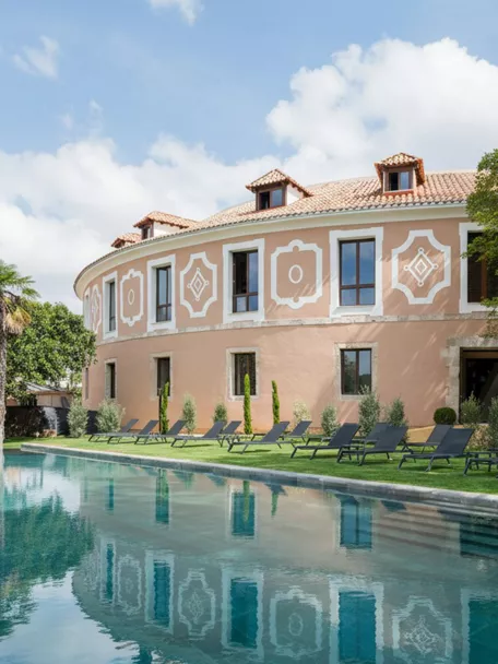 Fachada curva con piscina rectangular y tumbonas sobre césped.