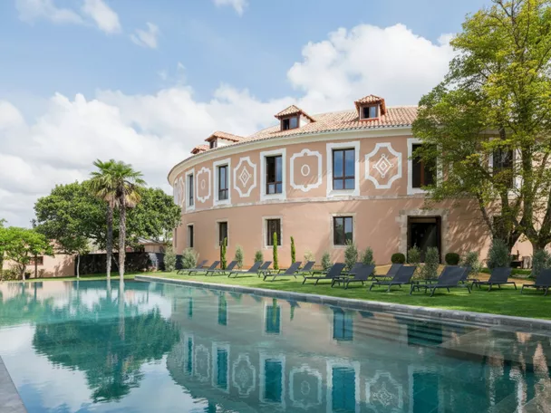 Fachada curva con piscina rectangular y tumbonas sobre césped.