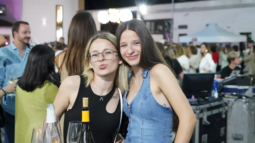 Dos mujeres sonríen junto a copas y una botella en una fiesta