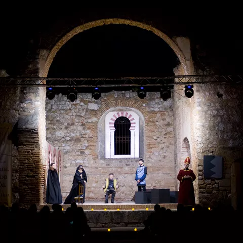 Representación teatral nocturna en escenario de piedra iluminado.