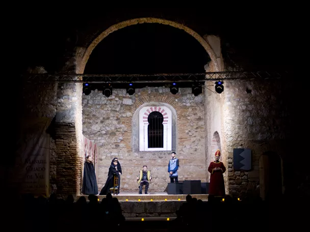Representación teatral nocturna en escenario de piedra iluminado.