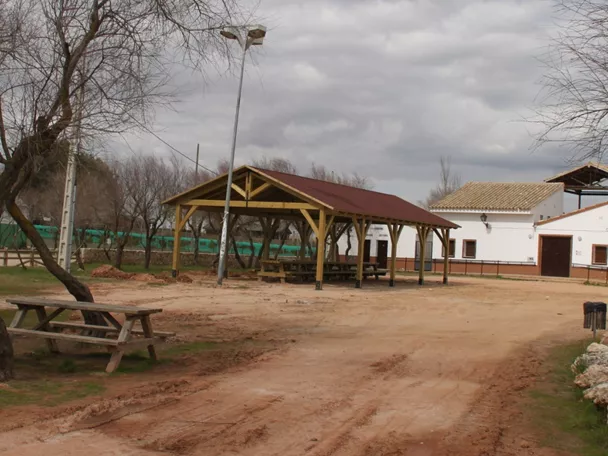 Área recreativa con mesas, porche de madera y edificio blanco.