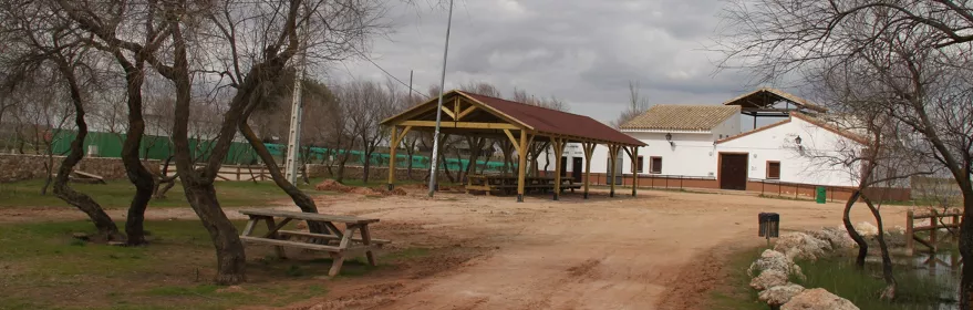 Área recreativa con mesas, porche de madera y edificio blanco.
