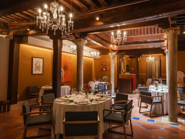 Salón elegante con mesas redondas, columnas de piedra y lámparas de araña.