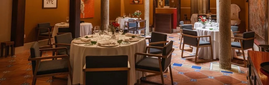 Salón elegante con mesas redondas, columnas de piedra y lámparas de araña.