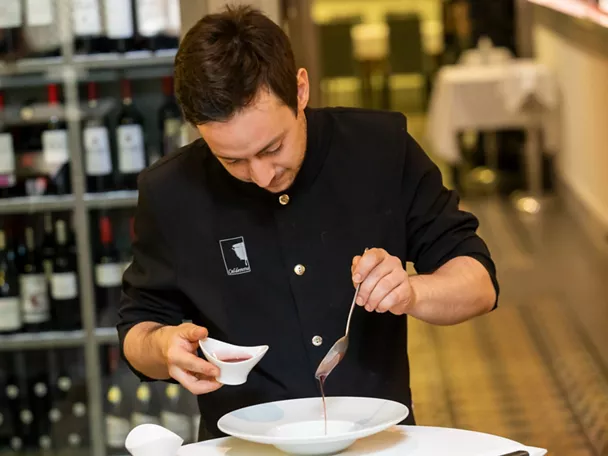 Chef sirviendo salsa sobre plato blanco