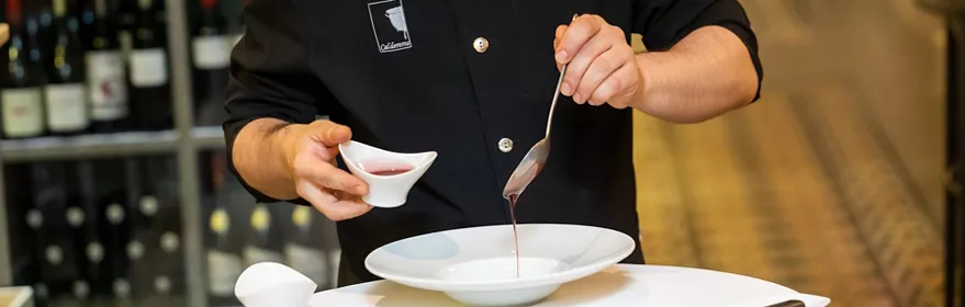 Chef sirviendo salsa sobre plato blanco