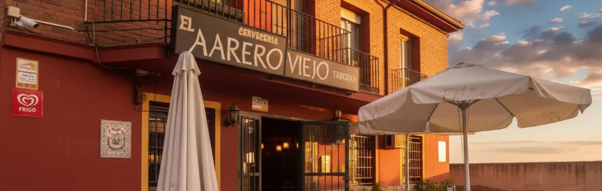 Entrada de taberna con sombrillas, barriles y fachada rojiza al atardecer.