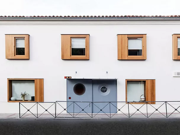 Fachada blanca con ventanas enmarcadas en madera y puerta gris.