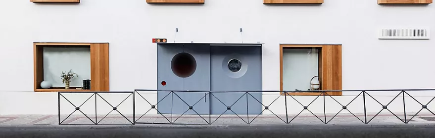 Fachada blanca con ventanas enmarcadas en madera y puerta gris.