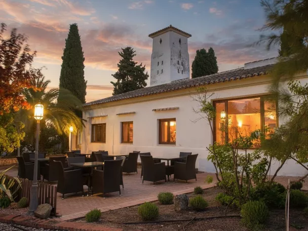 Terraza exterior con mesas y sillas junto a un edificio iluminado al atardecer.