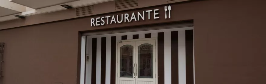 Fachada de restaurante con rótulo y puertas blancas, junto a una acera.