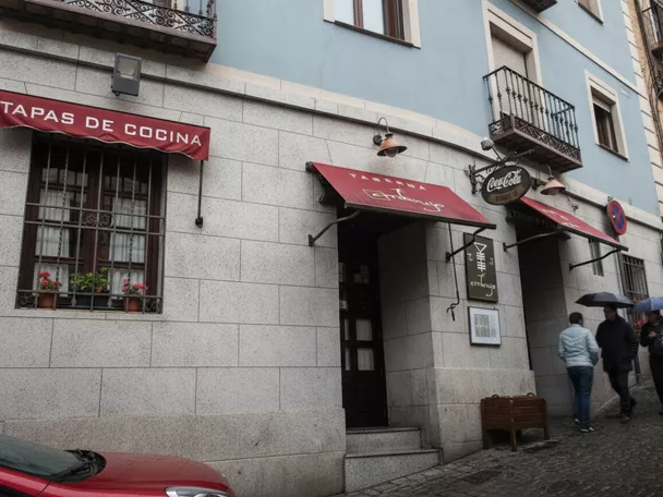 Fachada de restaurante con toldos rojos en calle adoquinada.