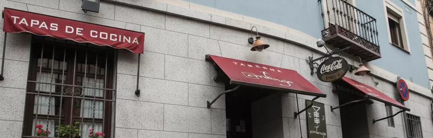 Fachada de restaurante con toldos rojos en calle adoquinada.