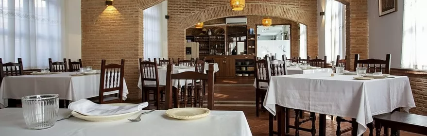 Salón de comedor amplio con arcos de ladrillo y manteles blancos.