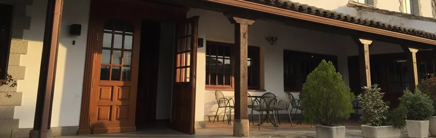 Fachada blanca de posada con porche, macetas y mesas exteriores.